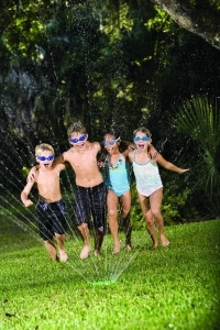 Children running through lawn sprinkler together