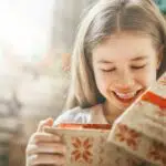 A young girl opening gifts for 7-9-year-olds at Christmas.