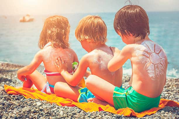 Little children applying sun protection lotion on the beach