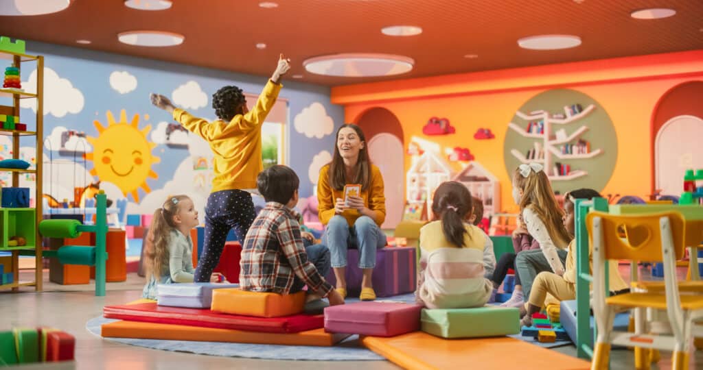 Cheerful childcare Teacher Using Gaming and Acting Methods to Teach Multiethnic Kids Alphabet in Kindergarten. Small Cute Boys and Girls Getting Basic Reading and Writing Skills, Learning Alphabet