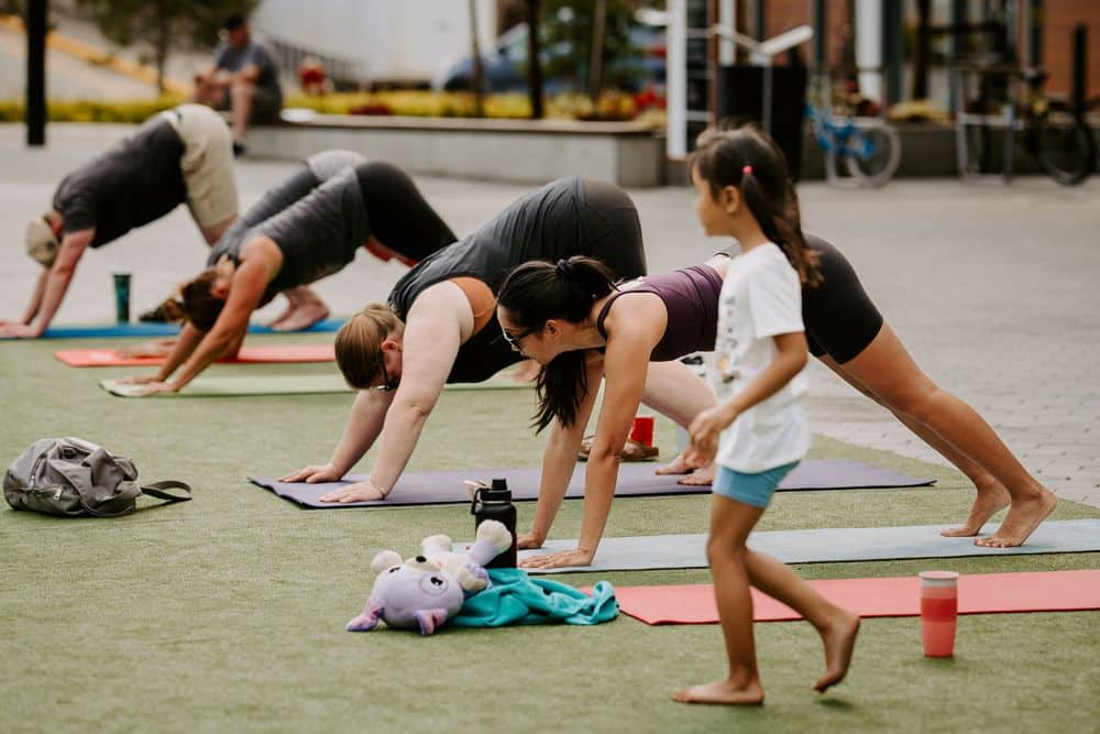 A girl watching people do yoga in an outdoor, public space.