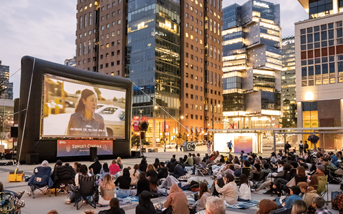 A crowd watching a movie on a big screen outside.