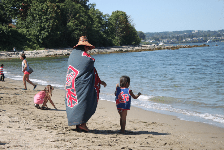Indigenous adult and child standing on the beach.